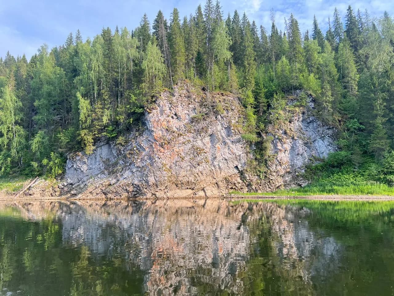 Известняковая стена камня-бойца с отражением в спокойной воде Чусовой